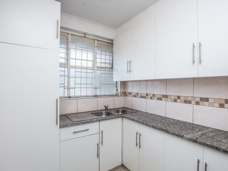 A functional kitchen featuring white cabinetry, granite countertops, a stainless steel double sink, and a tiled backsplash with decorative accents.