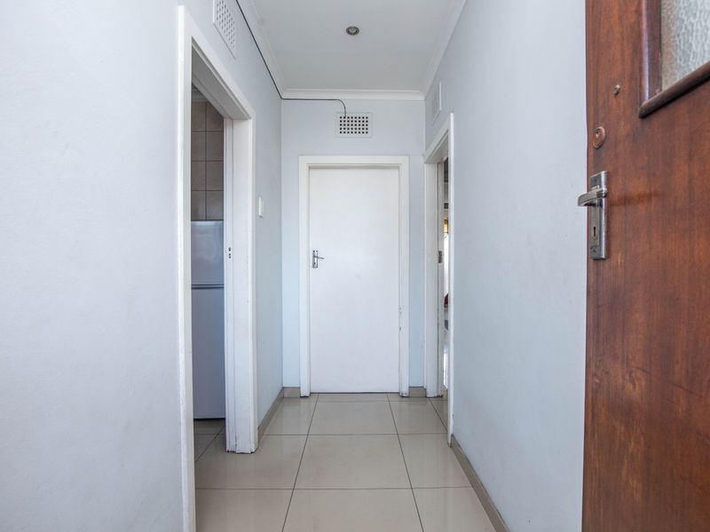 A clean, neutral hallway featuring tiled flooring and recessed lighting, providing access to multiple rooms within the apartment.