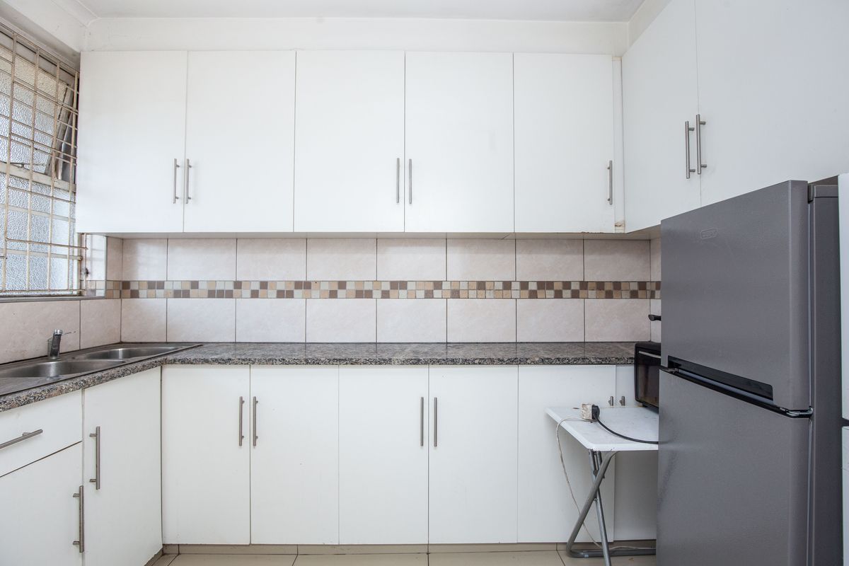 A functional kitchen featuring white cabinetry, granite countertops, a stainless steel double sink, and a tiled backsplash with decorative accents.