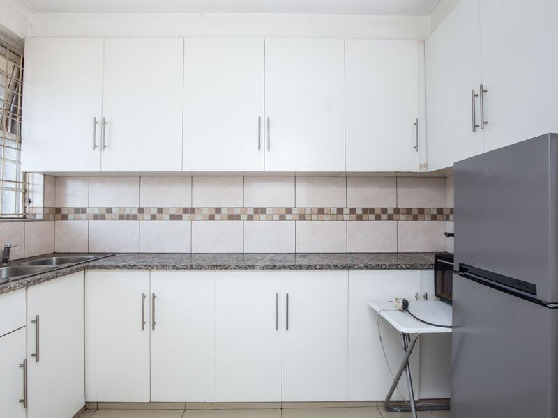A functional kitchen featuring white cabinetry, granite countertops, a stainless steel double sink, and a tiled backsplash with decorative accents.