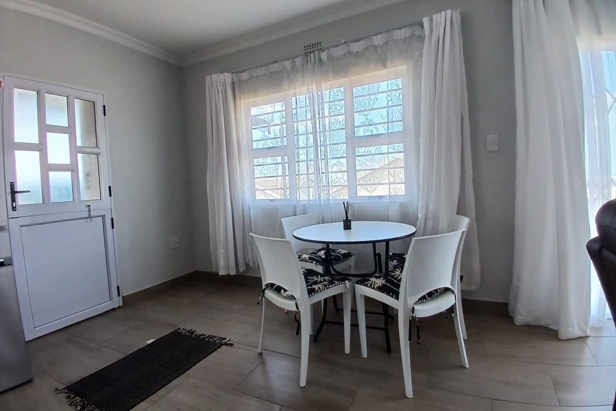 A bright living area featuring neutral tiled flooring, recessed downlights, and a secure entrance door with window security bars.