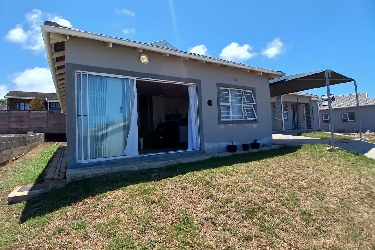 Rear view of a single-story house featuring a sliding door entrance, a carport, and a grassed yard area.