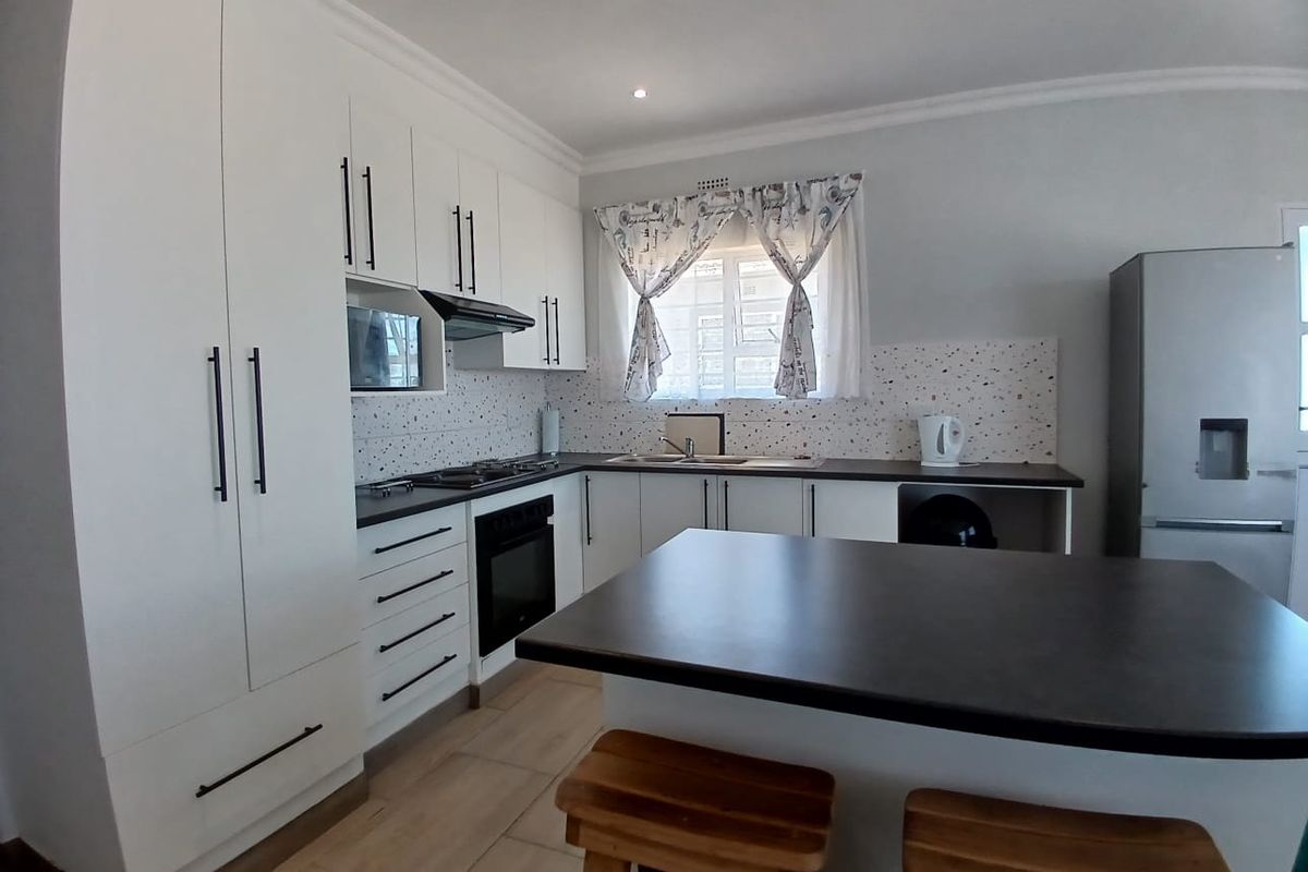 Modern kitchen featuring white cabinetry, dark countertops, a central island, built-in oven, gas hob, and a stylish terrazzo-style backsplash.