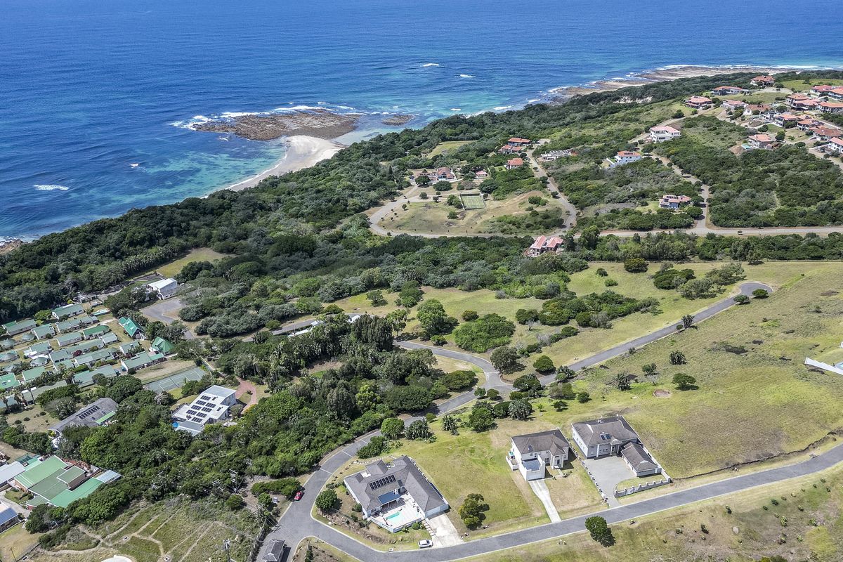 An aerial view of a coastal residential estate featuring established road infrastructure, surrounding natural vegetation, and proximity to the ocean.