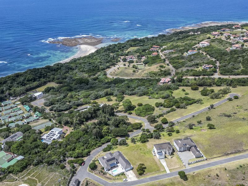 An aerial view of a coastal residential estate featuring established road infrastructure, surrounding natural vegetation, and proximity to the ocean.