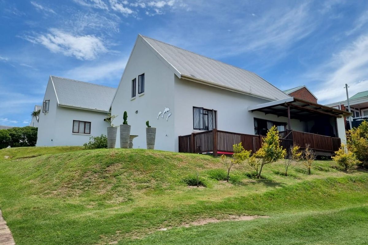 Rear view of a townhouse featuring a metal roof, a raised timber deck with a covered patio area, and well-maintained lawn.