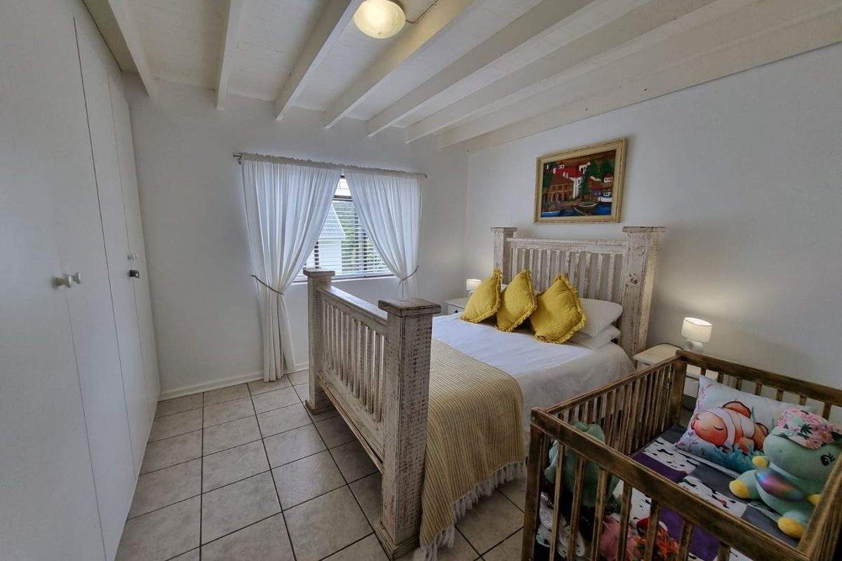 A bedroom featuring tiled flooring, built-in cupboards, and an exposed beam ceiling, providing a functional and well-lit living space.