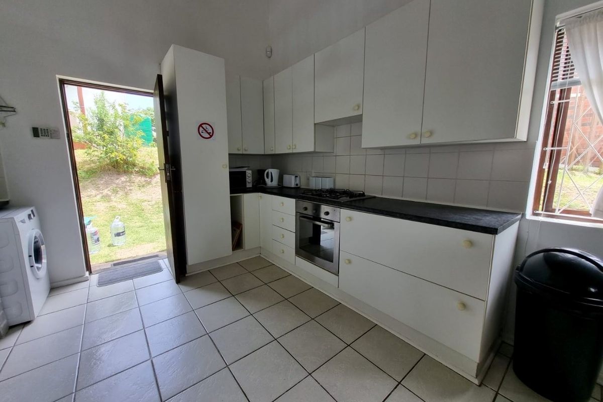 Functional kitchen featuring white cabinetry, dark laminate countertops, built-in oven and gas hob, tiled flooring, and direct access to the rear garden.