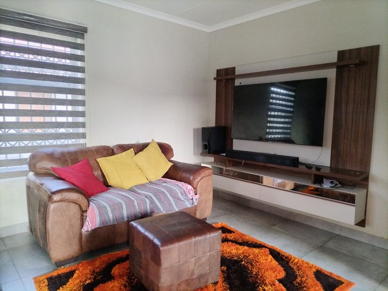 A comfortable living room featuring a modern built-in media unit, tiled flooring, and large windows with roller blinds.