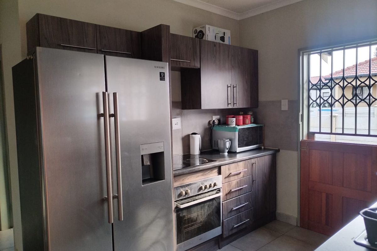 A functional kitchen featuring dark wood-look cabinetry, built-in oven and hob, and tiled flooring, with a security gate on the exterior door.