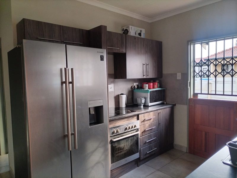 A functional kitchen featuring dark wood-look cabinetry, built-in oven and hob, and tiled flooring, with a security gate on the exterior door.