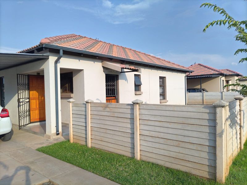 Front exterior view of a single-story residential house featuring a tiled roof, paved driveway, and a precast concrete boundary wall.