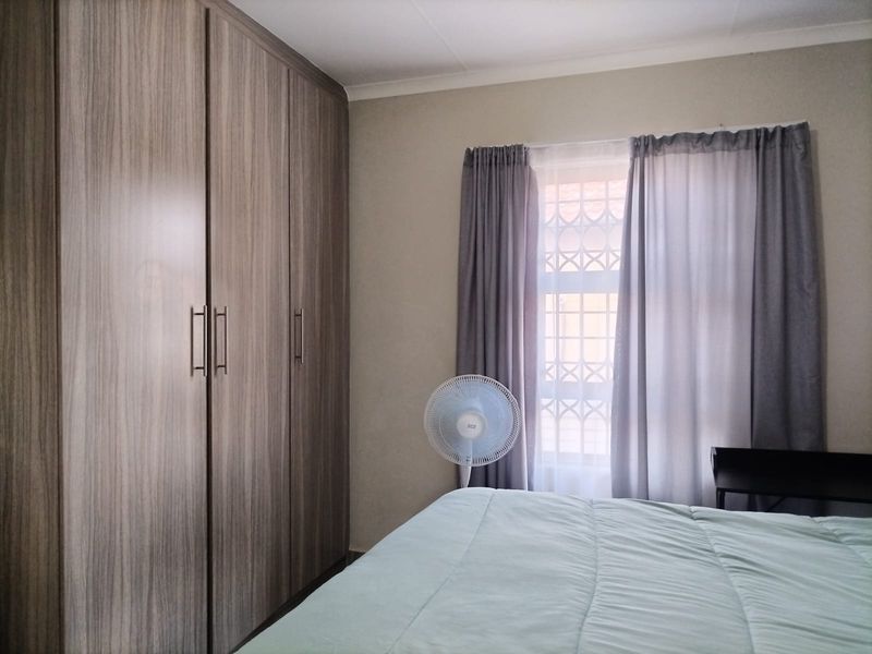A well-maintained bedroom featuring modern wood-grain built-in cupboards and a window fitted with security bars.