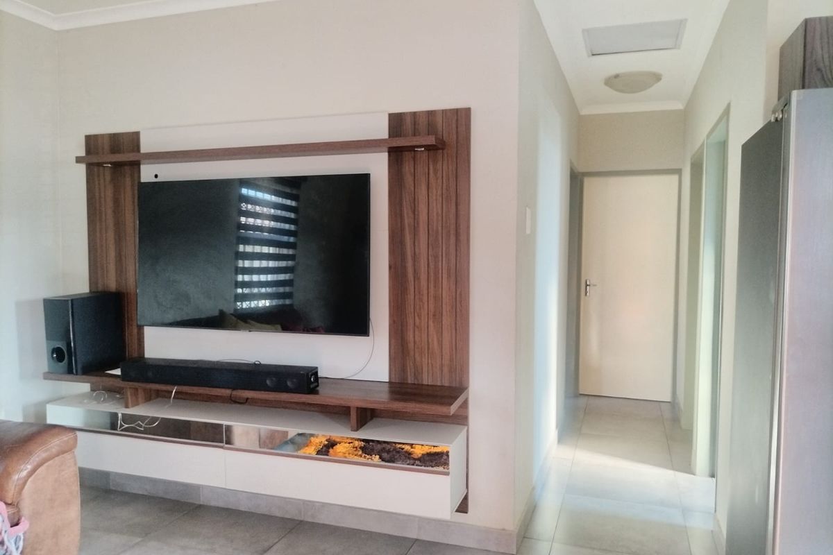 A living room featuring a modern built-in media unit with wood-look paneling and tiled flooring, leading into a hallway.