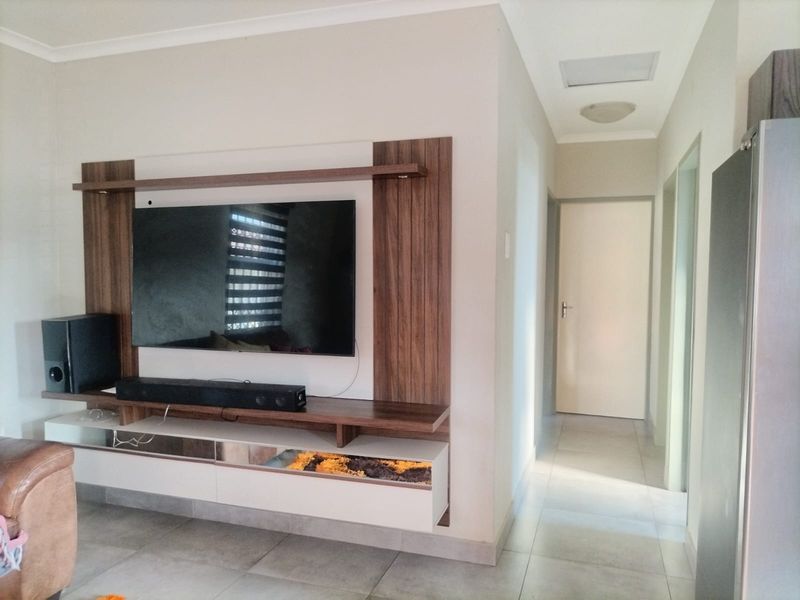 A living room featuring a modern built-in media unit with wood-look paneling and tiled flooring, leading into a hallway.