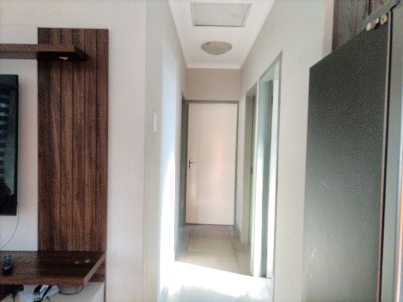 A bright, neutral hallway featuring tiled flooring, built-in wooden shelving, and access to multiple rooms.