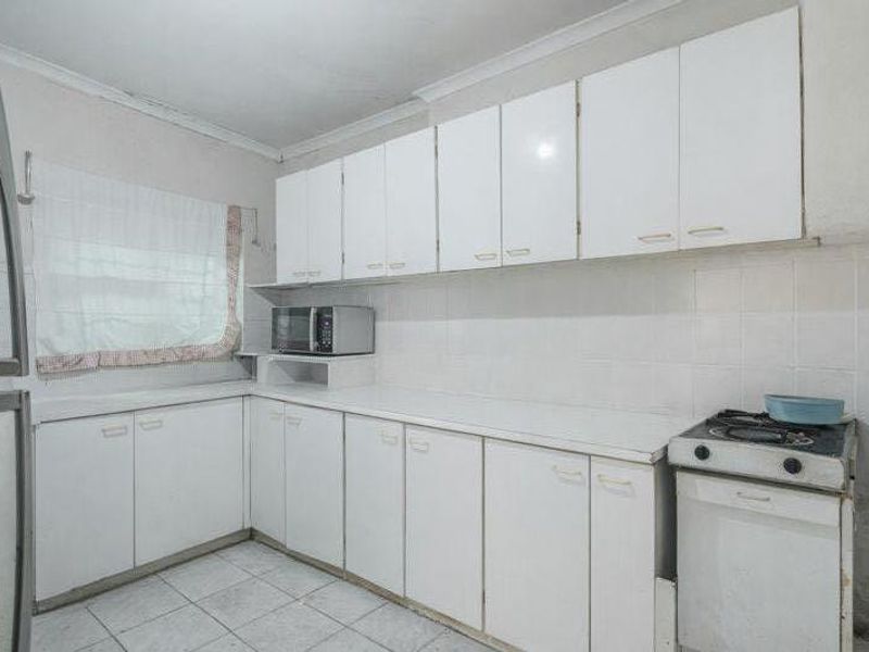 A functional kitchen featuring white cabinetry, tiled backsplash, and tiled flooring, offering a dated aesthetic with potential for modern renovation.