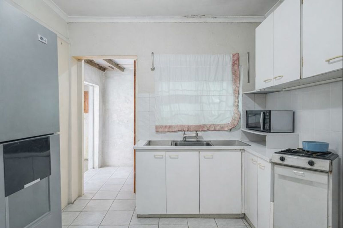A functional kitchen featuring white cabinetry, a stainless steel sink, gas stove, and tiled flooring, leading into an adjacent utility area.