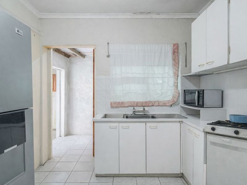 A functional kitchen featuring white cabinetry, a stainless steel sink, gas stove, and tiled flooring, leading into an adjacent utility area.