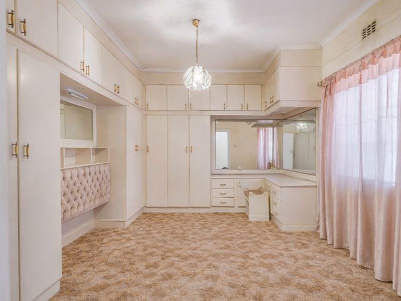 Spacious bedroom featuring extensive built-in cabinetry, a dedicated vanity area with integrated mirrors, and neutral carpeting.