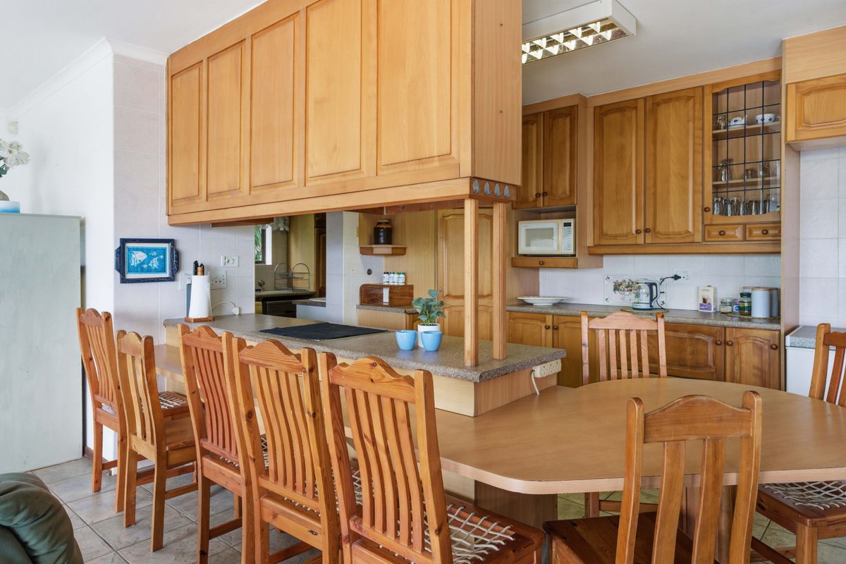 A functional kitchen featuring traditional timber cabinetry, a breakfast bar with integrated seating, and tiled flooring, offering a classic layout with ample storage space.