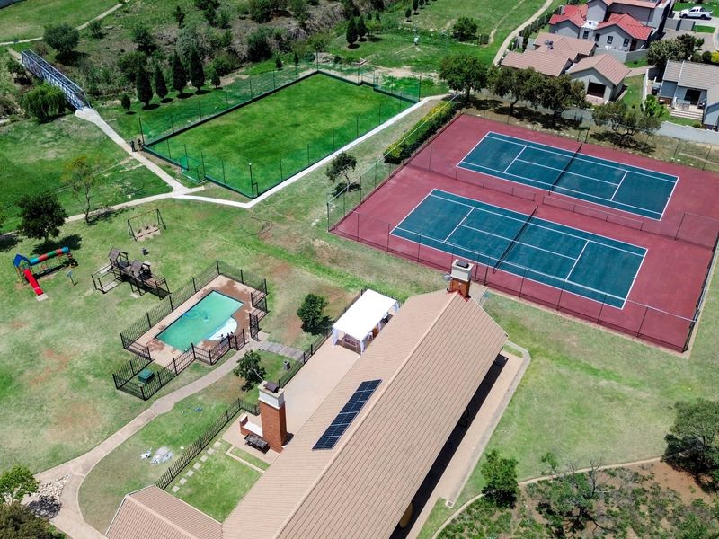 Aerial view of the estate clubhouse featuring tennis courts, a swimming pool, playground, and landscaped grounds with solar panels installed on the roof.