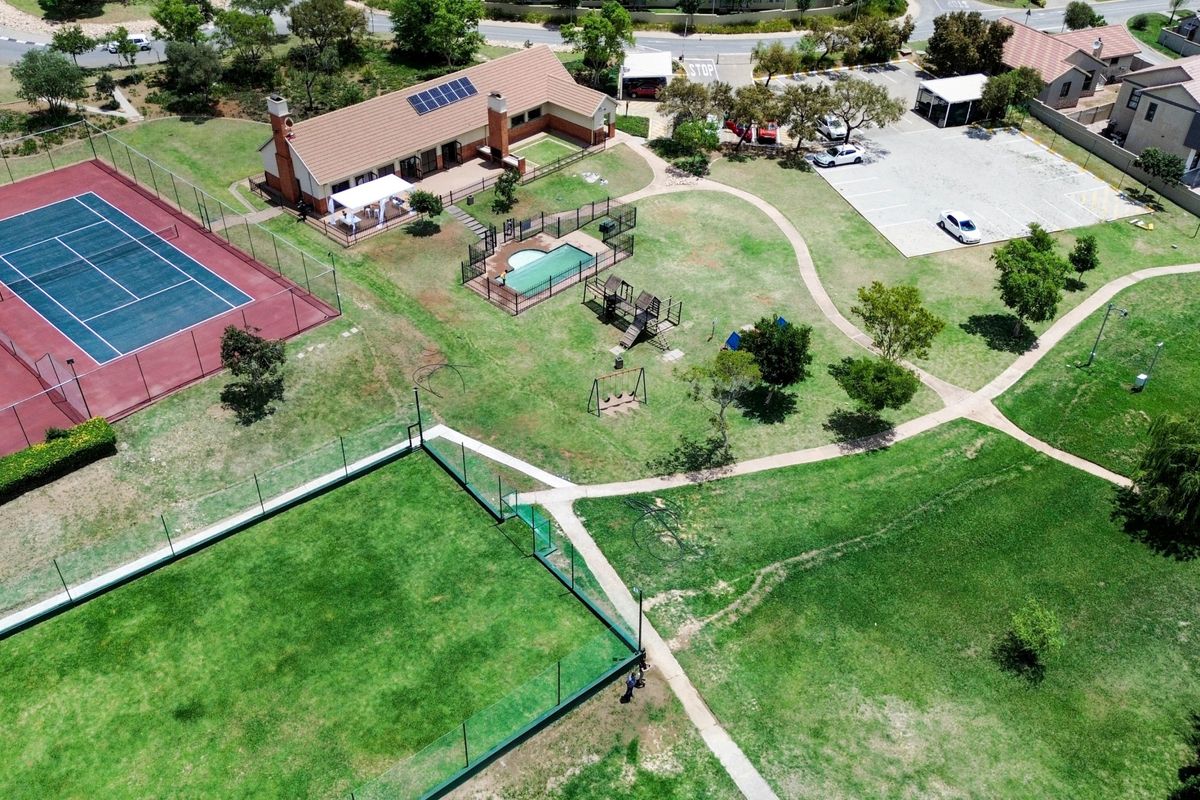 Aerial view of the apartment complex grounds featuring a tennis court, swimming pool, playground, parking area, and well-maintained landscaped gardens.