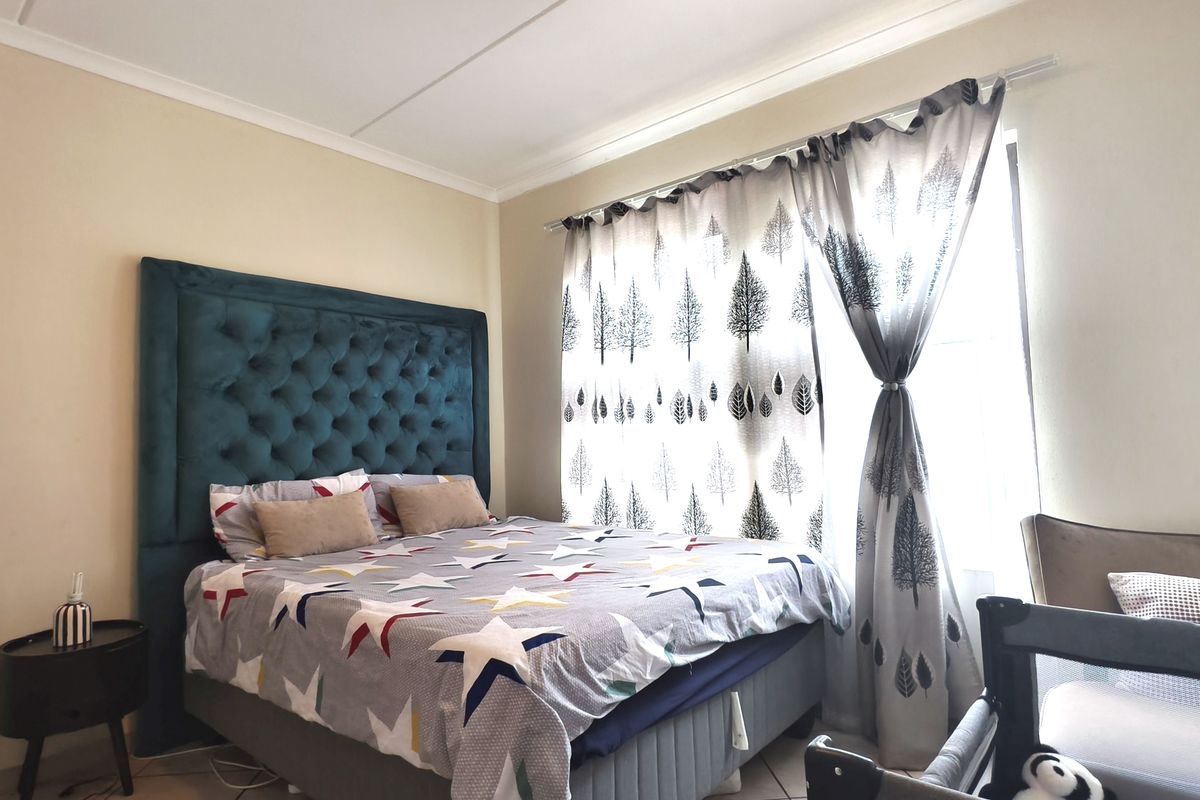 A well-lit bedroom featuring tiled flooring, coved ceilings, and a large window with decorative curtains.