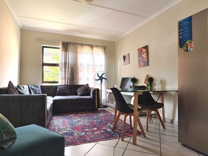 An open-plan living and dining area featuring tiled flooring, coved ceilings, and a large window providing natural light.