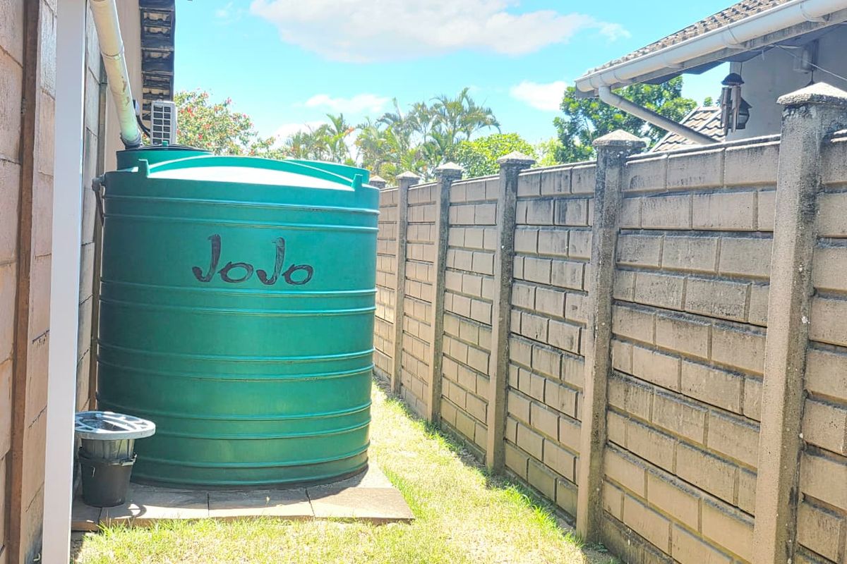 Side yard area featuring a large green water storage tank and a precast concrete boundary wall.