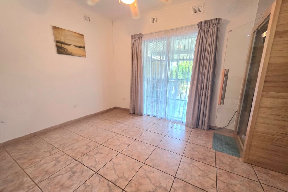 A spacious bedroom featuring tiled flooring, a ceiling fan, and a sliding glass door providing access to the exterior, with an integrated sauna unit.