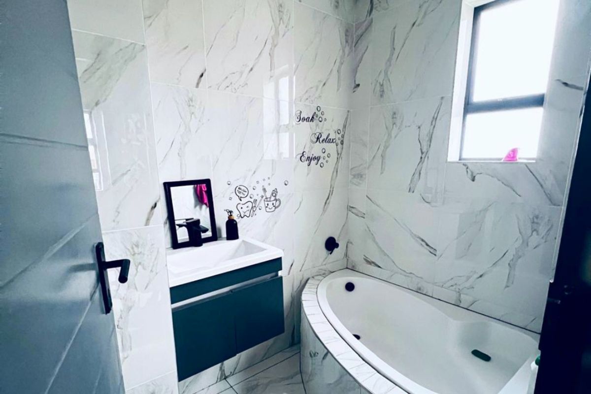 Modern bathroom featuring floor-to-ceiling marble-look tiling, a built-in bathtub, and a wall-mounted vanity unit with a basin.