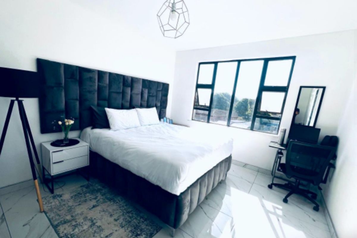 A bright and modern bedroom featuring large windows, polished tile flooring, and a contemporary geometric pendant light fixture.