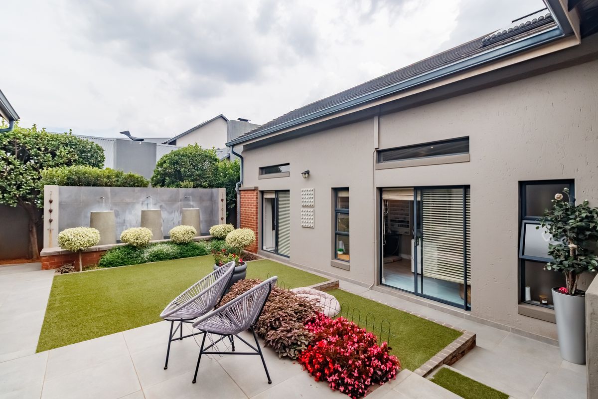 A well-maintained rear courtyard featuring a tiled patio, artificial lawn, and a modern water feature, with direct access to the home via sliding doors.