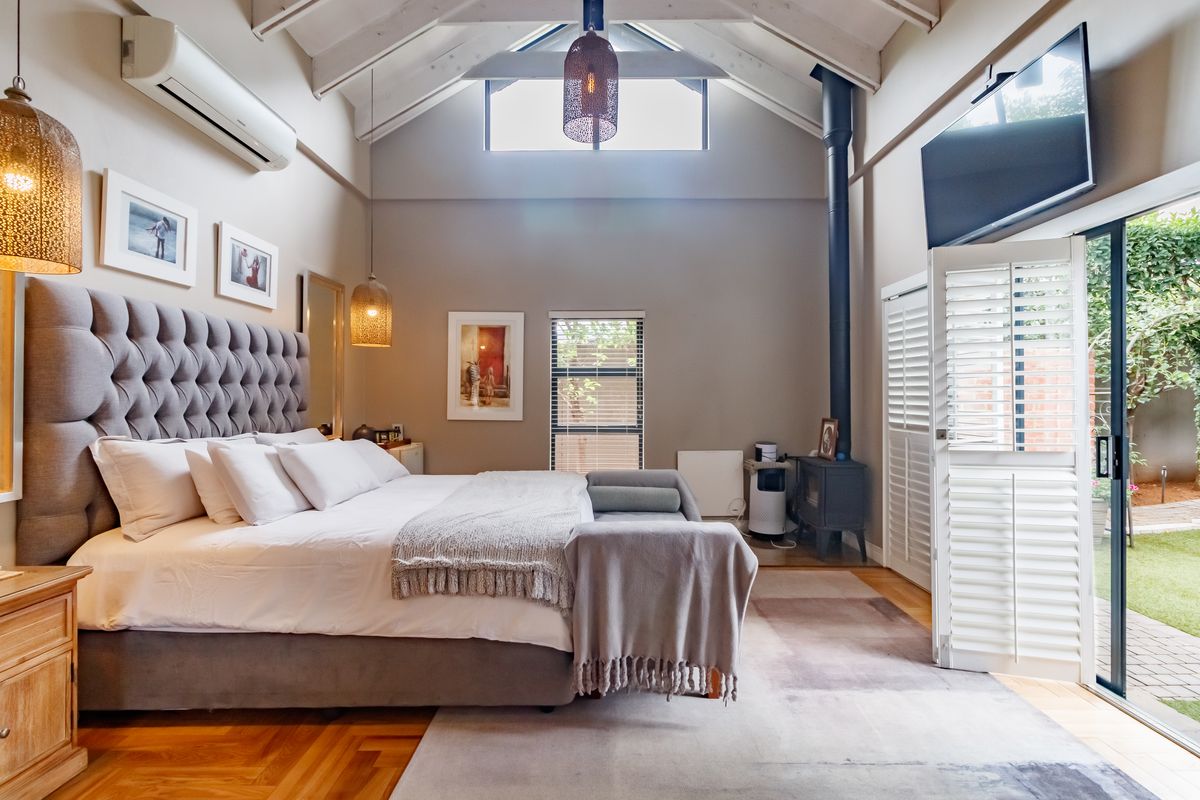 Spacious bedroom featuring a vaulted ceiling with exposed beams, wood-burning stove, timber flooring, and direct access to the garden through sliding glass doors.
