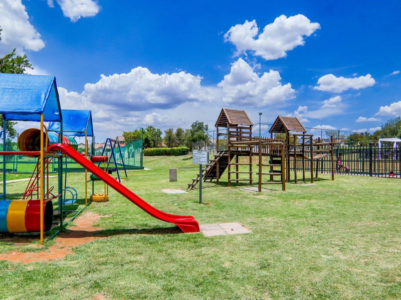 A well-maintained communal playground area featuring various climbing structures, slides, and secure perimeter fencing within the apartment complex grounds.