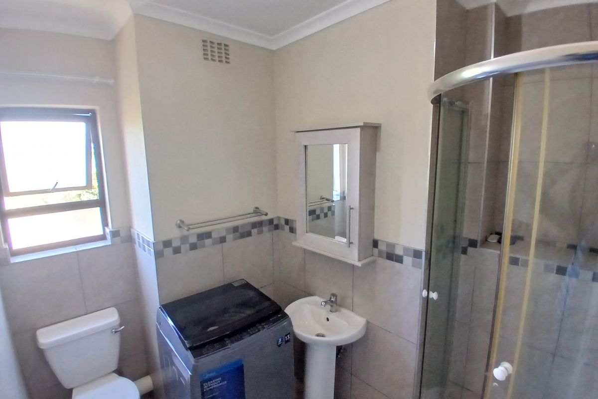 A functional bathroom featuring a pedestal basin, toilet, and a glass-enclosed shower with neutral wall tiling and a wall-mounted medicine cabinet.