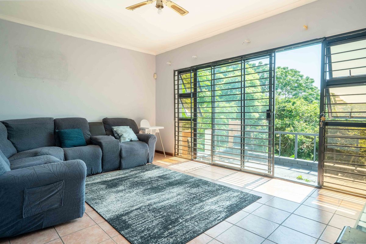 A living room featuring tiled flooring, a ceiling fan, and large sliding glass doors with security bars opening to an outdoor balcony area.
