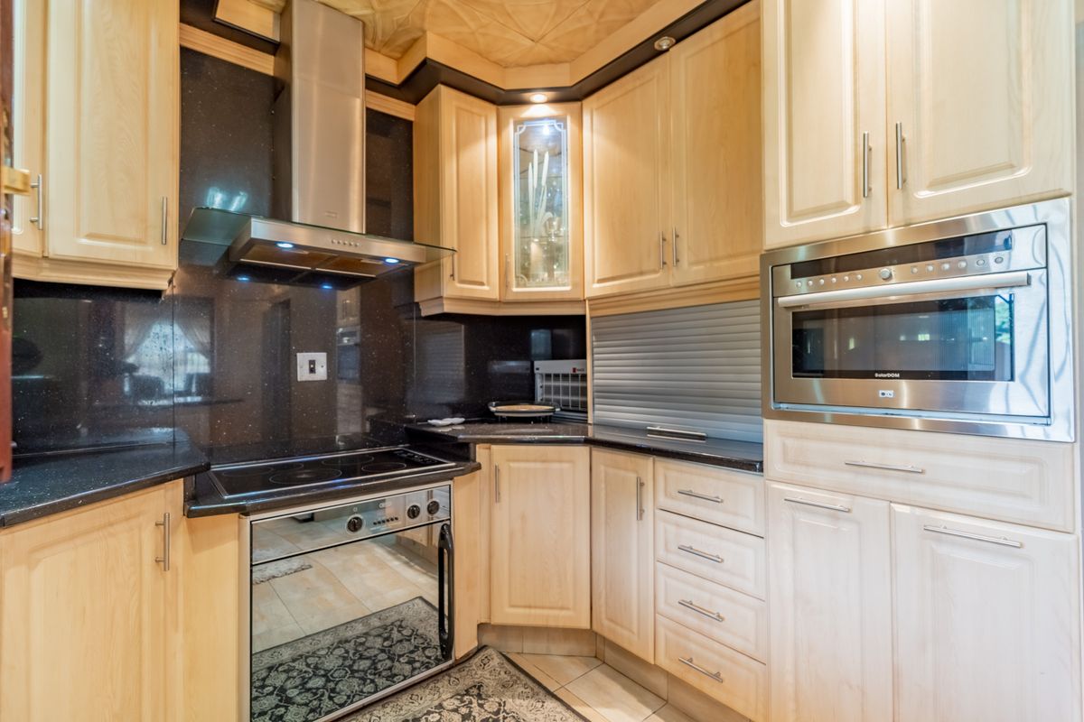 A well-maintained kitchen featuring light wood cabinetry, dark granite countertops, integrated appliances, and a stainless steel extractor fan.