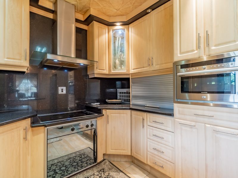 A well-maintained kitchen featuring light wood cabinetry, dark granite countertops, integrated appliances, and a stainless steel extractor fan.