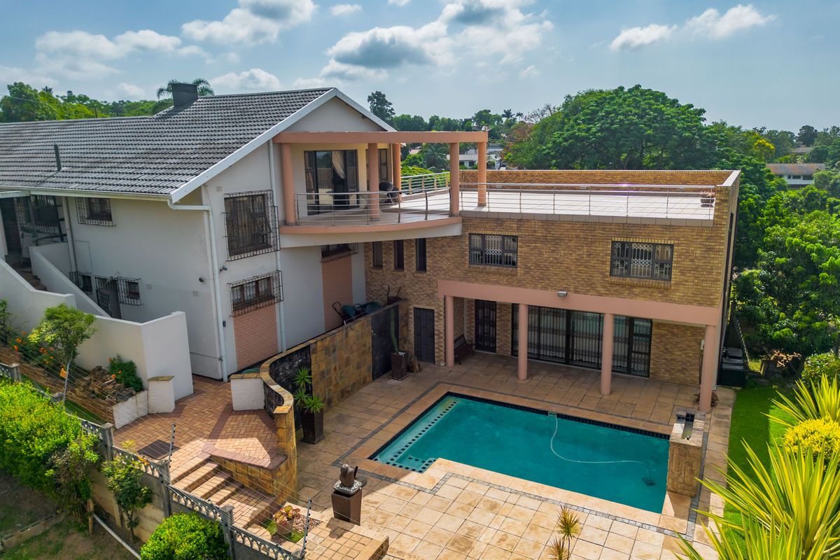 Aerial view of the rear exterior featuring a swimming pool, paved patio area, upper-level balcony, and a mix of brick and rendered wall finishes.
