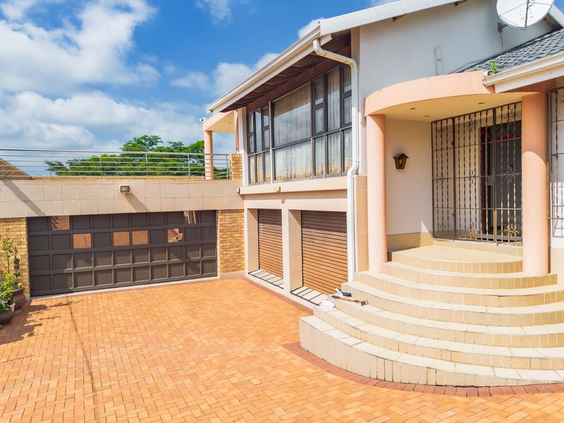 Front exterior view featuring a paved driveway, multiple garage doors, and a raised entrance with tiled steps and security gate.