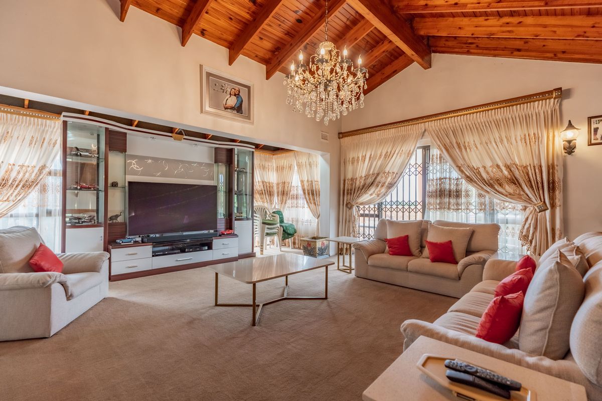 Spacious living room featuring a high vaulted timber ceiling with exposed beams, a crystal chandelier, and custom built-in display cabinetry.