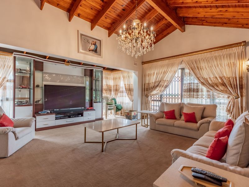 Spacious living room featuring a high vaulted timber ceiling with exposed beams, a crystal chandelier, and custom built-in display cabinetry.