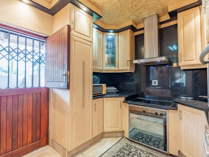 A well-maintained kitchen featuring light-wood cabinetry, black granite countertops, a built-in oven with extractor fan, and a traditional stable door with security gate.