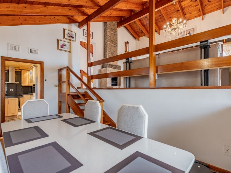 Open plan living and dining area featuring a vaulted timber ceiling, stone fireplace, and a mezzanine level with a timber staircase.