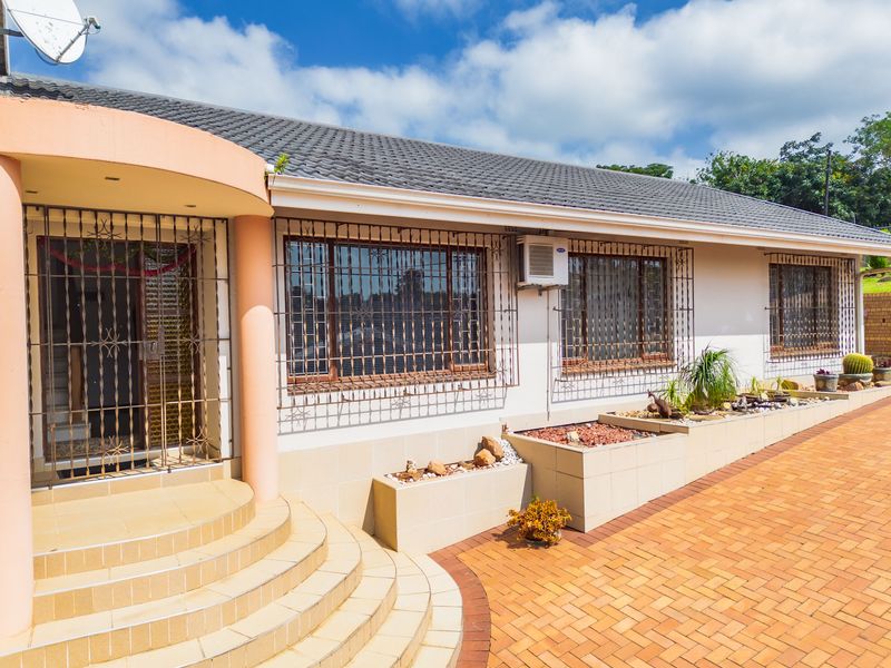 Front facade of a single-story house featuring tiled entrance steps, security bars on windows, and integrated tiled planter boxes along the paved driveway.
