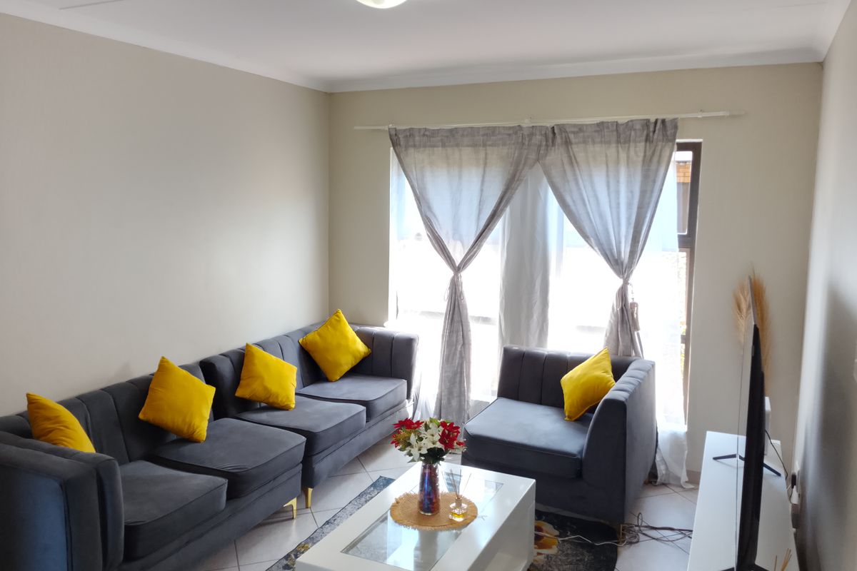 A well-lit living room featuring neutral wall tones, tiled flooring, and a large window with curtain fittings, providing a comfortable and functional living space.