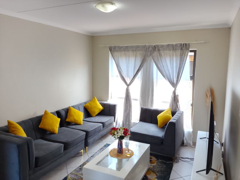 A well-lit living room featuring neutral wall tones, tiled flooring, and a large window with curtain fittings, providing a comfortable and functional living space.