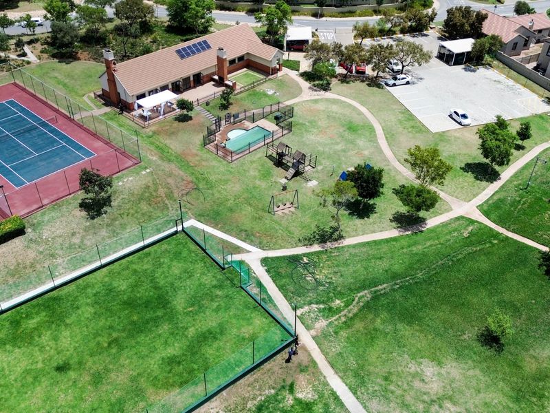 Aerial view of the apartment complex grounds featuring a tennis court, swimming pool, playground, parking area, and well-maintained landscaped gardens.